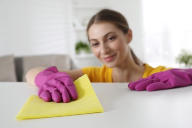 Young woman cleaning table with rag in office, selective focus