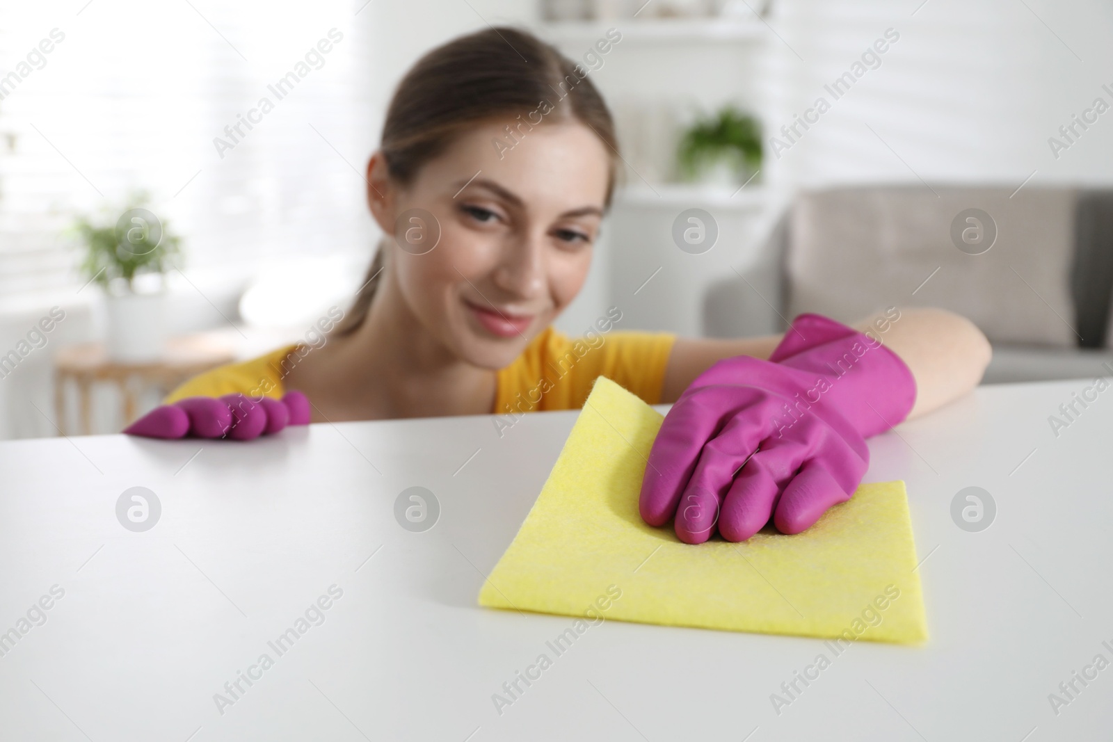 Photo of Young woman cleaning table with rag in office, selective focus