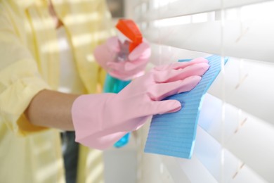 Photo of Young woman cleaning window blinds with rag and spray at home, closeup