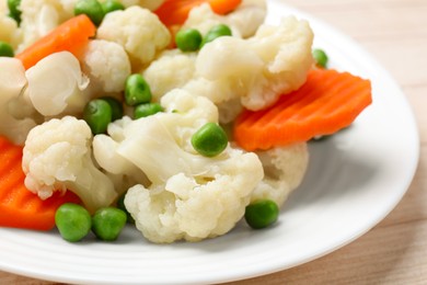 Photo of Tasty cooked cauliflower with green peas and carrot slices on white wooden table, closeup