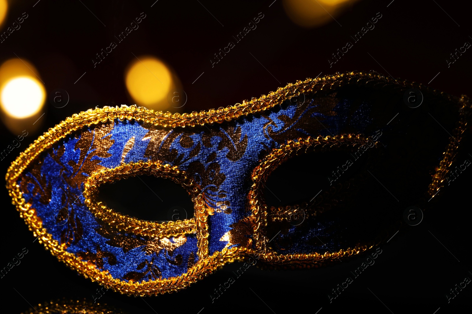 Photo of Beautiful blue carnival mask on black background, closeup. Bokeh effect