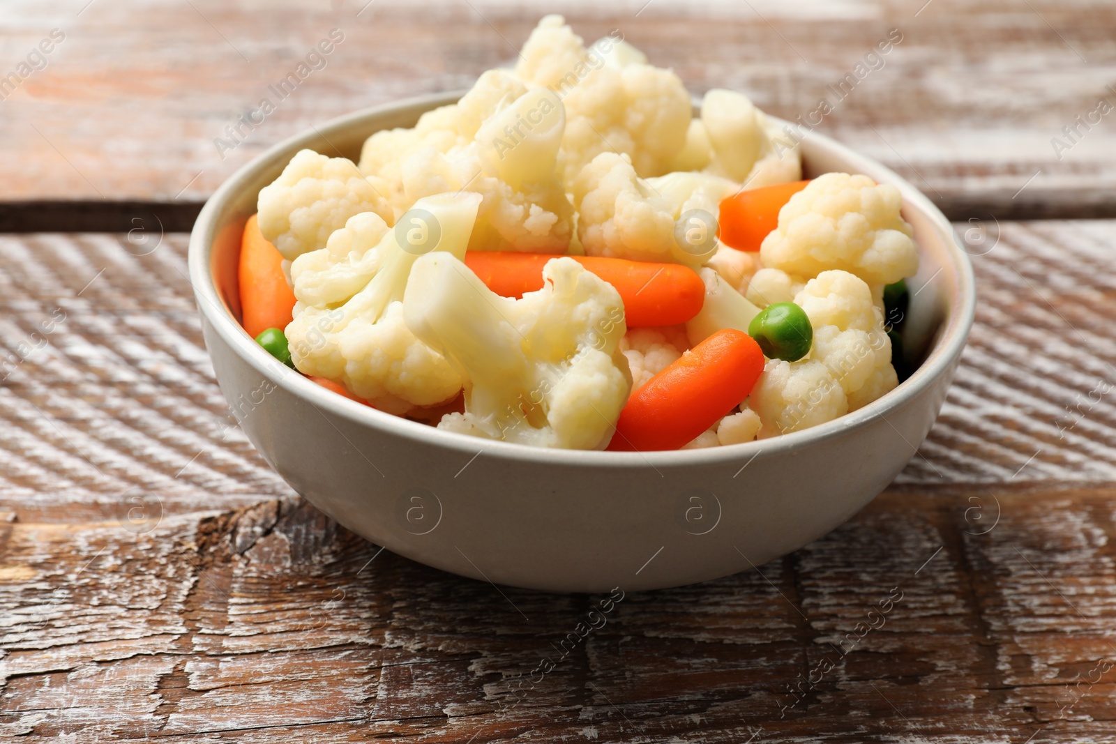 Photo of Tasty cauliflower with baby carrots and green peas on wooden table, closeup