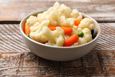 Photo of Tasty cauliflower with baby carrots and green peas on wooden table, closeup