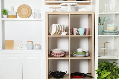 Photo of Shelving units with kitchenware near white wall indoors