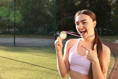 Happy winner pointing at golden medal at stadium. Space for text