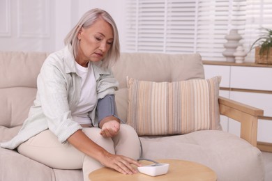 Woman measuring blood pressure on sofa indoors