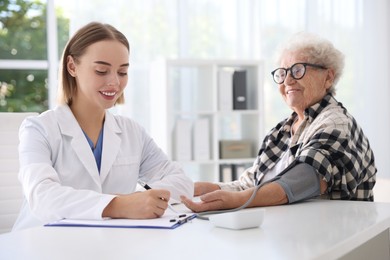 Doctor measuring patient's blood pressure at table in hospital