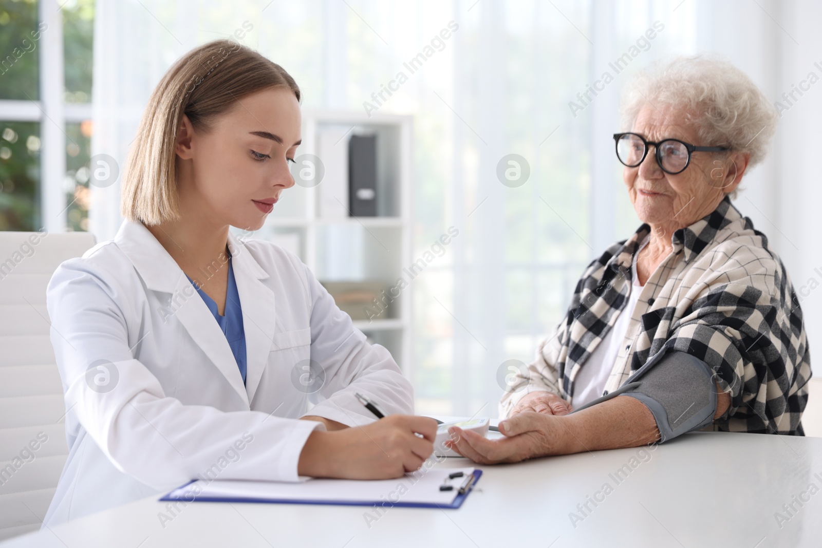 Photo of Doctor measuring patient's blood pressure at table in hospital