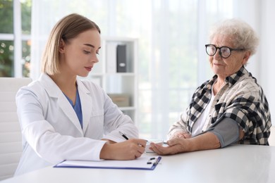 Photo of Doctor measuring patient's blood pressure at table in hospital