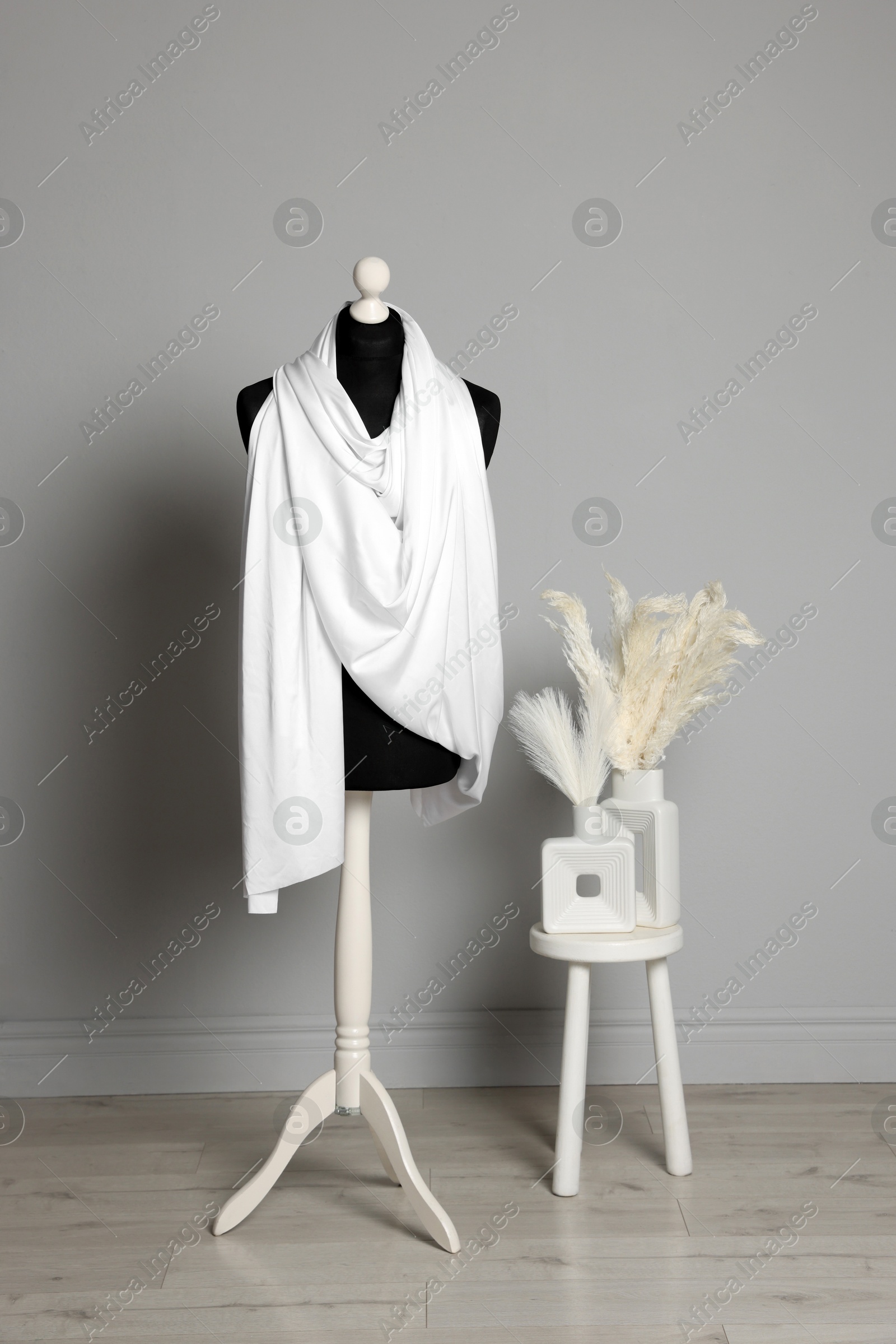 Photo of Female mannequin with white scarf near gray wall indoors