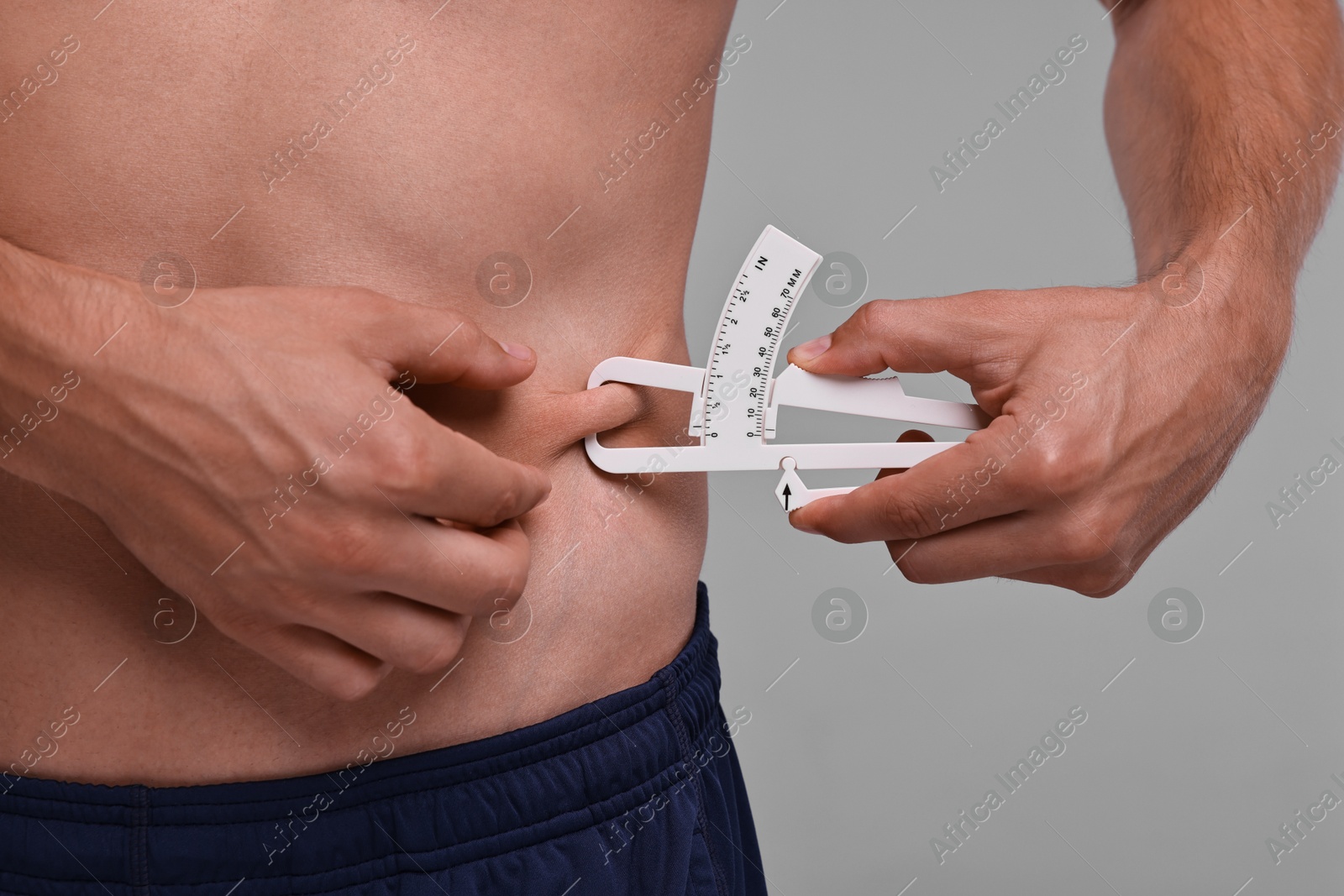 Photo of Man measuring body fat with caliper on grey background, closeup