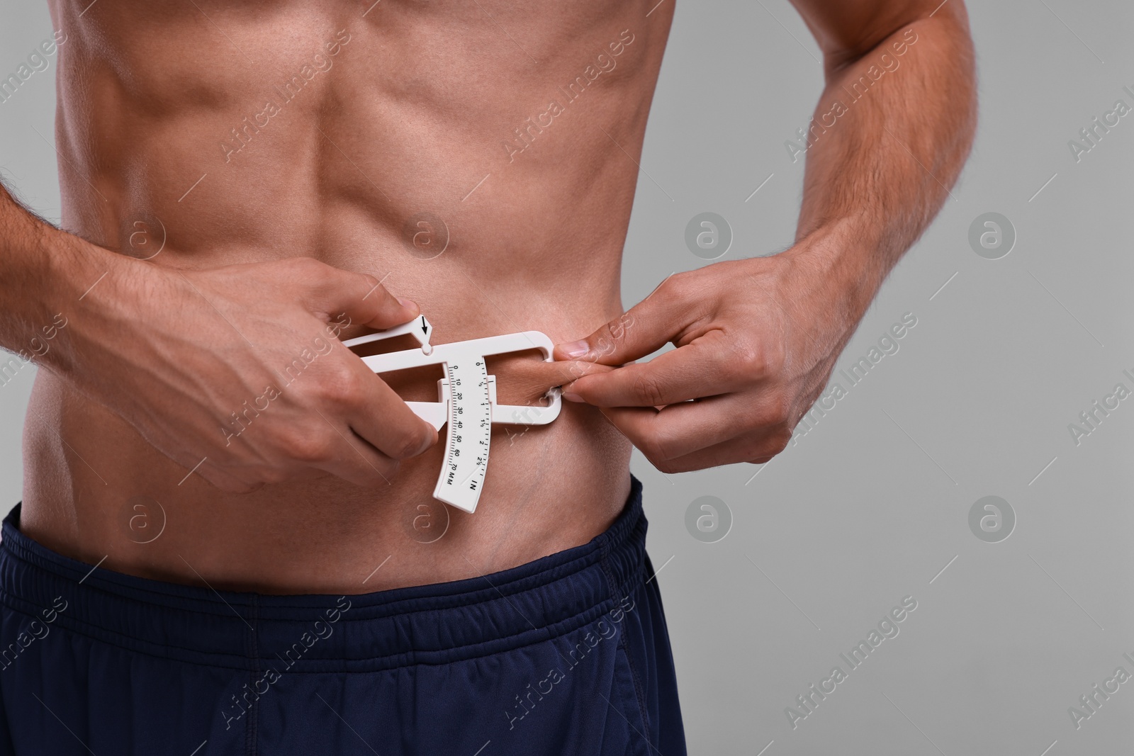 Photo of Man measuring body fat with caliper on grey background, closeup