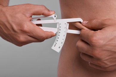 Photo of Man measuring body fat with caliper on grey background, closeup