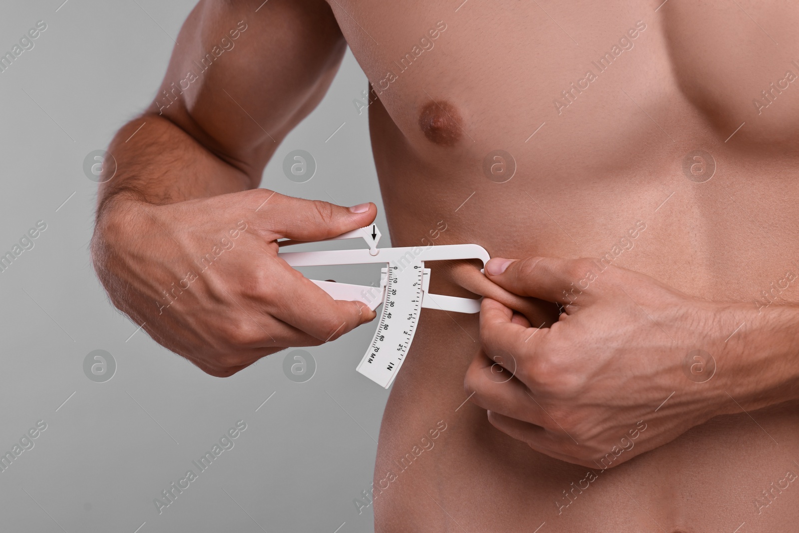 Photo of Man measuring body fat with caliper on grey background, closeup