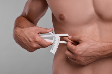 Photo of Man measuring body fat with caliper on grey background, closeup