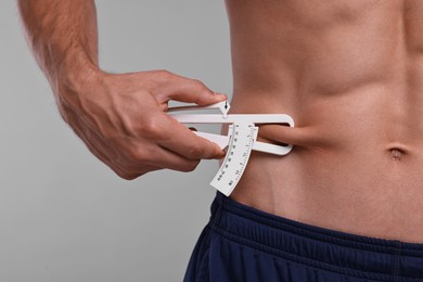 Photo of Man measuring body fat with caliper on grey background, closeup