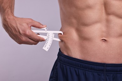 Photo of Man measuring body fat with caliper on grey background, closeup