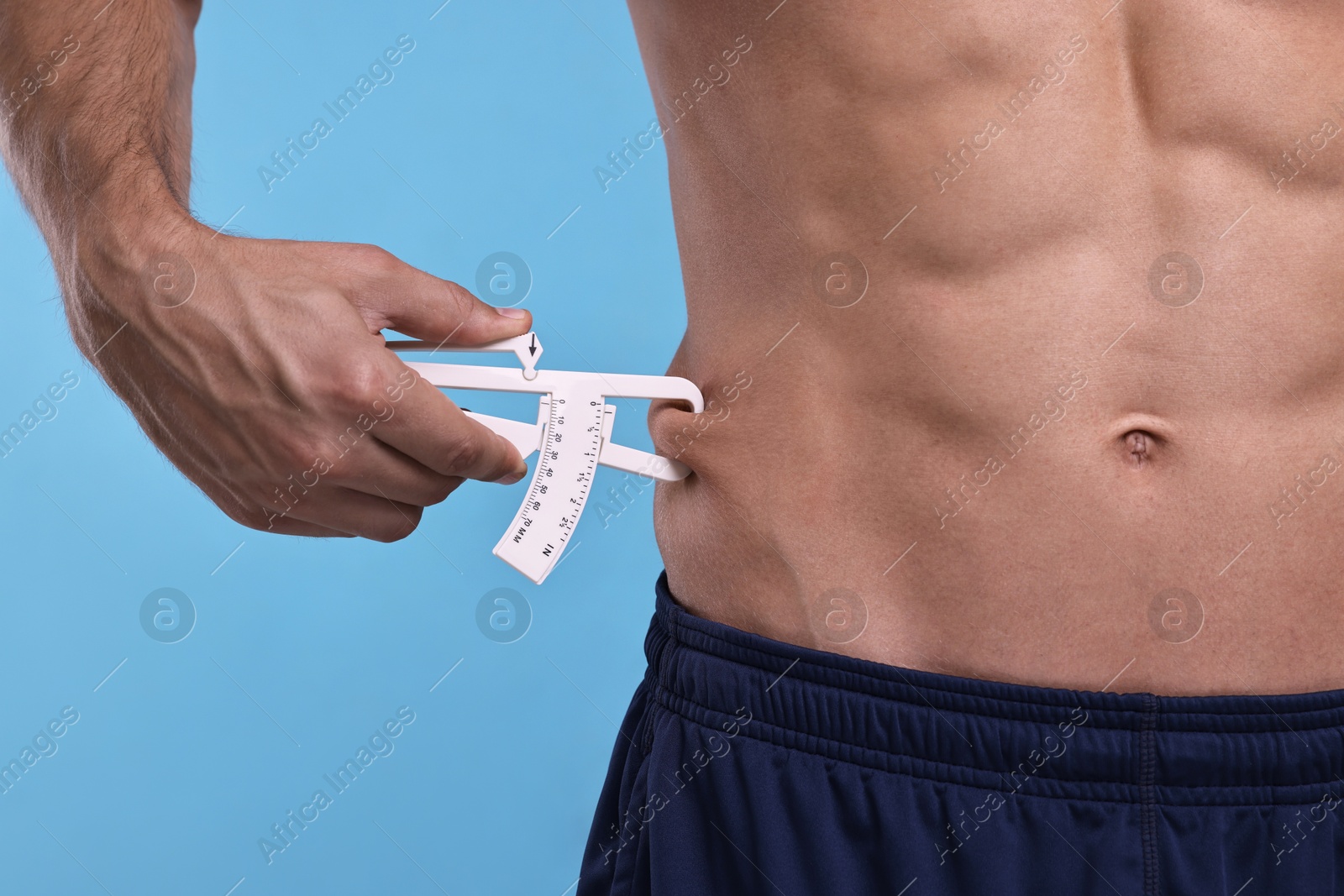 Photo of Man measuring body fat with caliper on light blue background, closeup