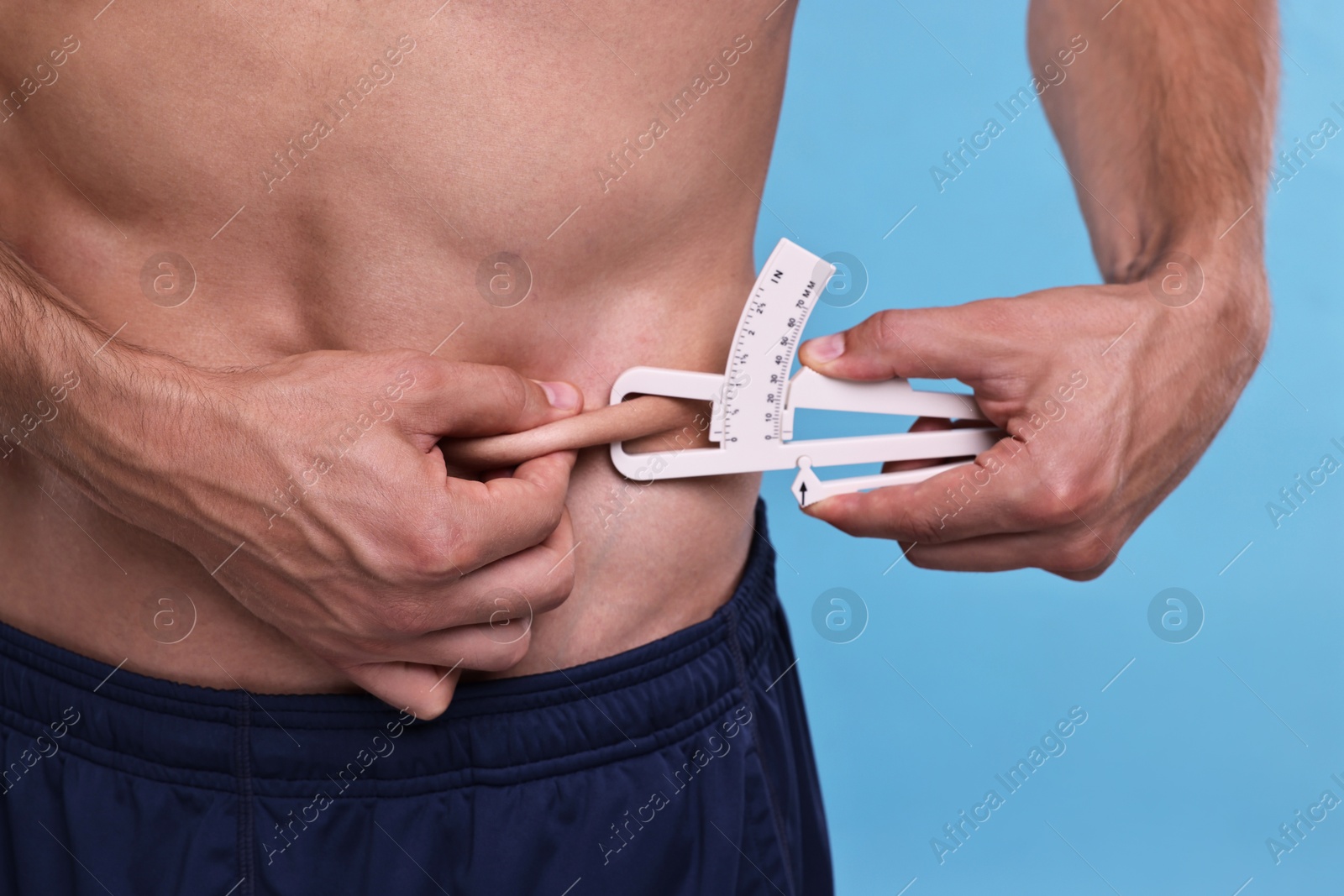 Photo of Man measuring body fat with caliper on light blue background, closeup