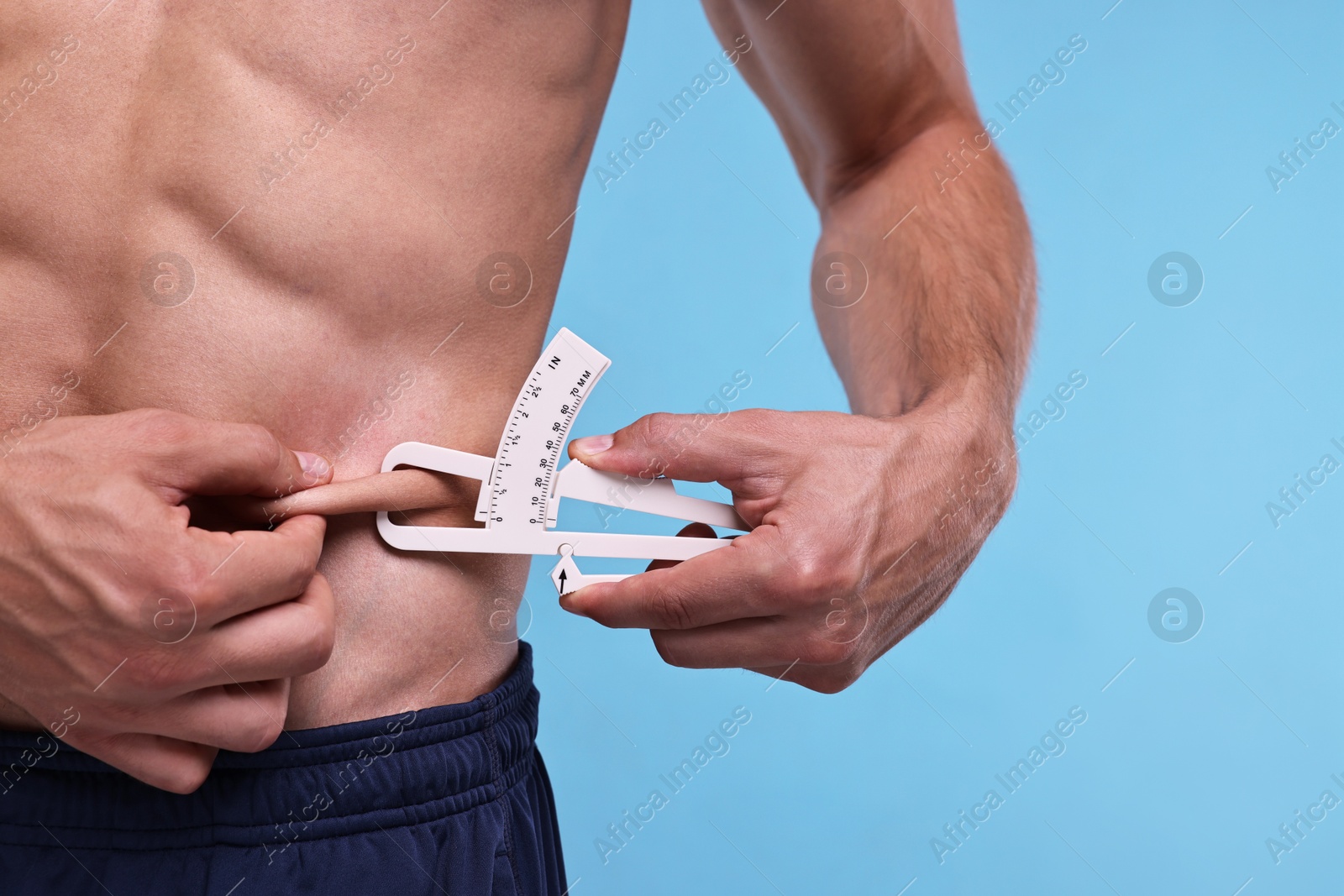 Photo of Man measuring body fat with caliper on light blue background, closeup