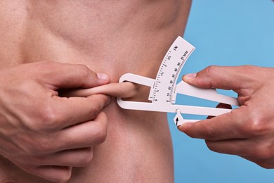 Photo of Man measuring body fat with caliper on light blue background, closeup