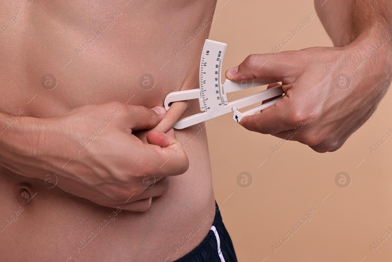 Photo of Man measuring body fat with caliper on beige background, closeup