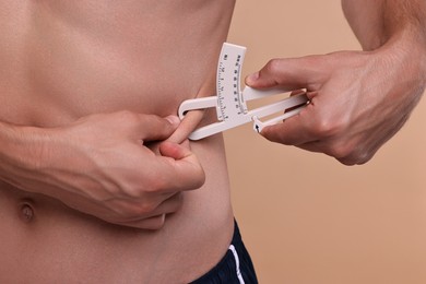 Photo of Man measuring body fat with caliper on beige background, closeup