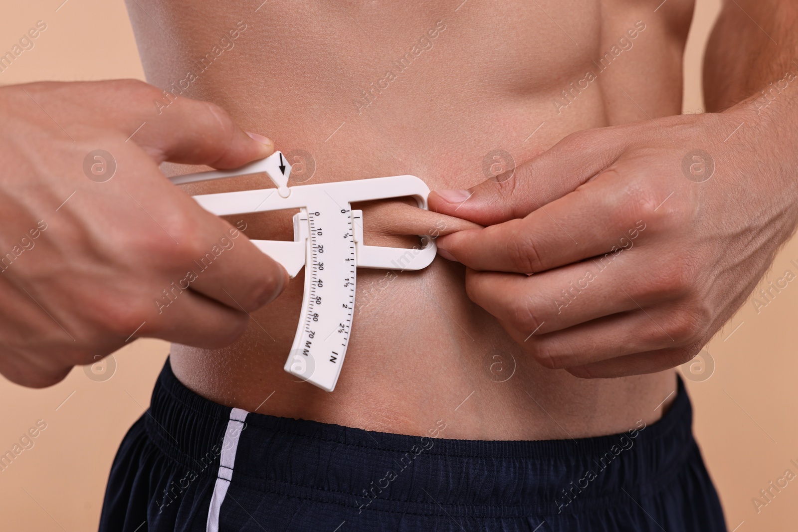 Photo of Man measuring body fat with caliper on beige background, closeup