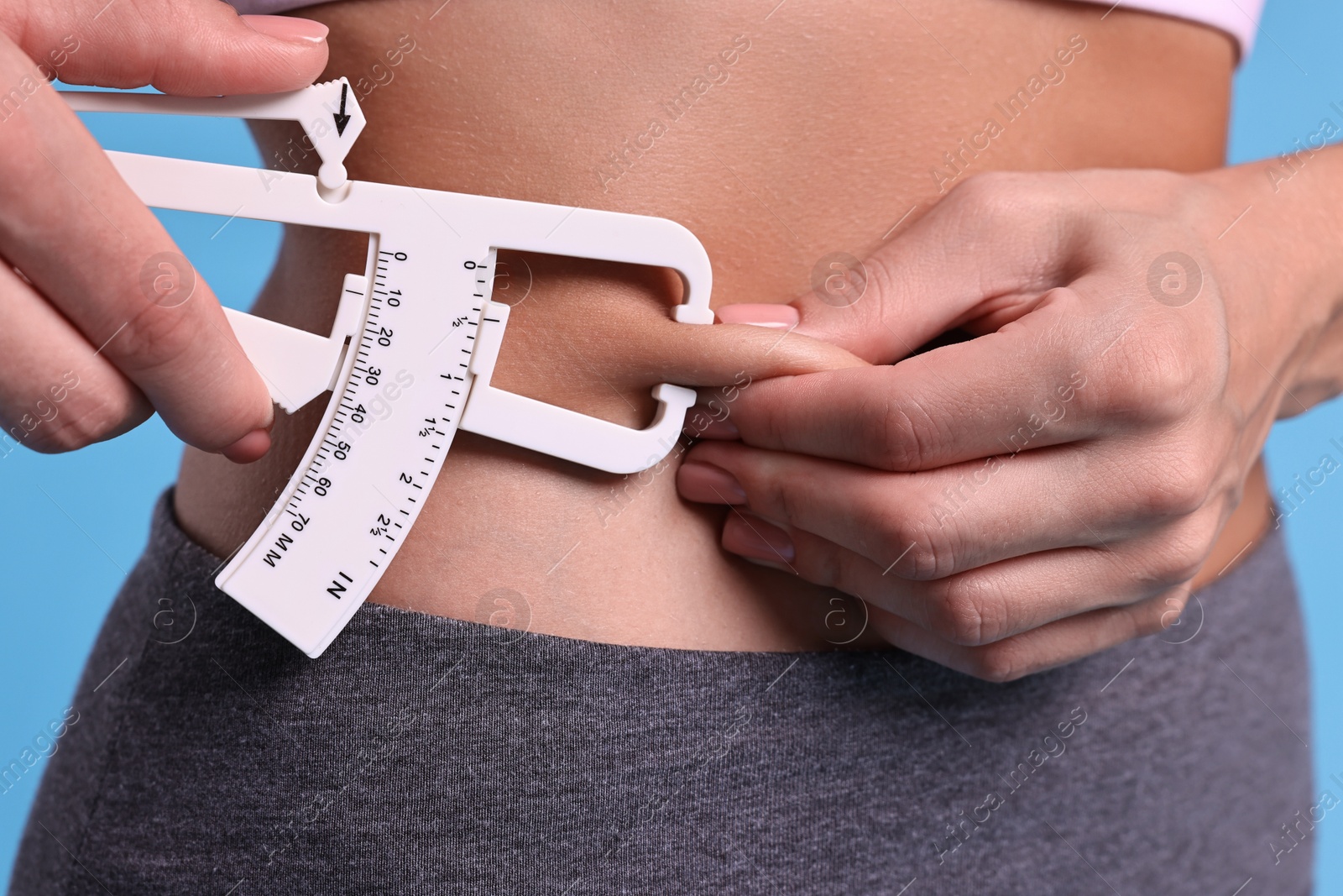 Photo of Woman measuring body fat with caliper on light blue background, closeup