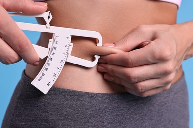 Photo of Woman measuring body fat with caliper on light blue background, closeup