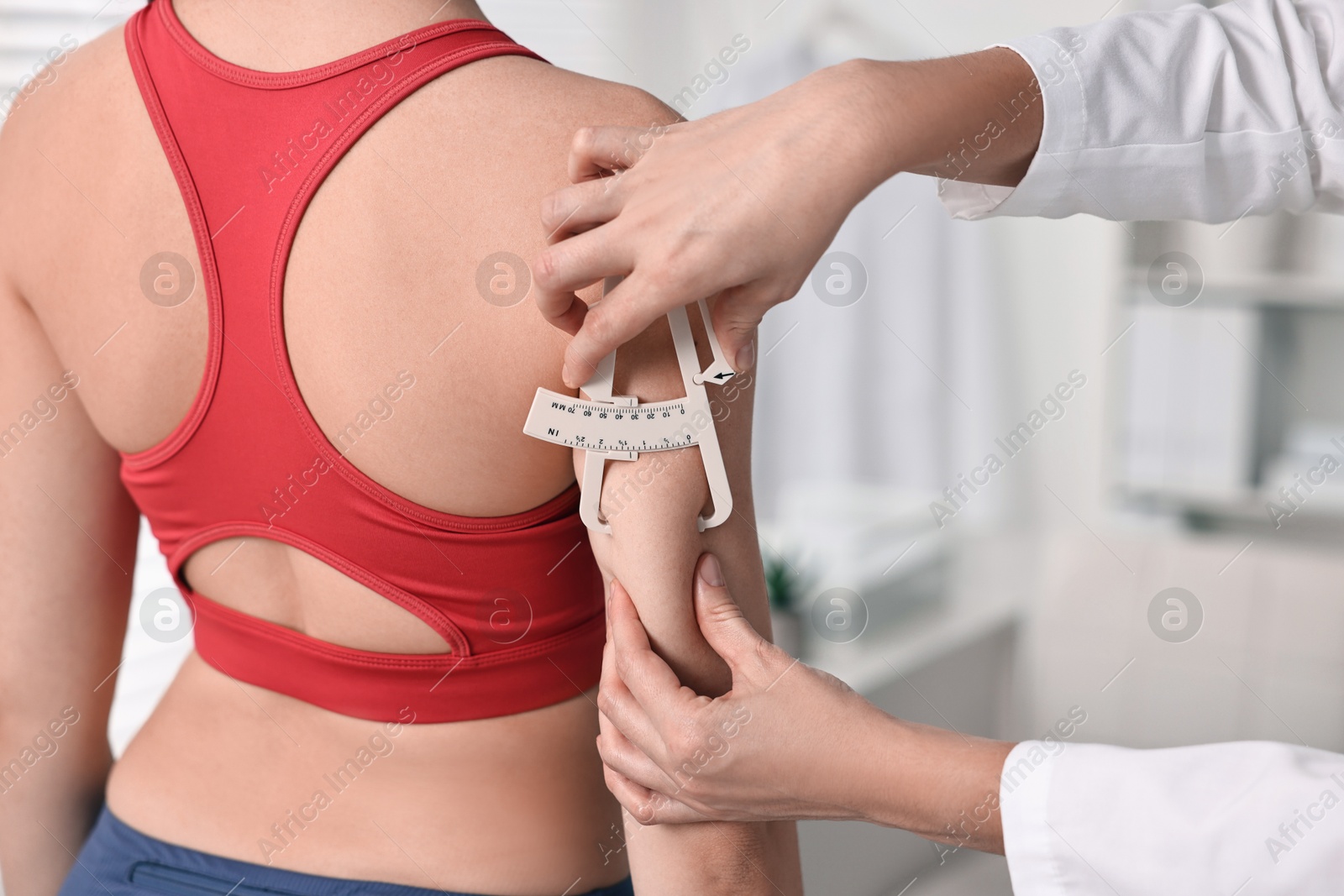 Photo of Doctor measuring woman's body fat with caliper in clinic, closeup