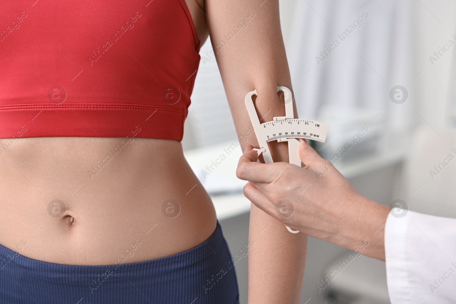 Photo of Doctor measuring woman's body fat with caliper in clinic, closeup