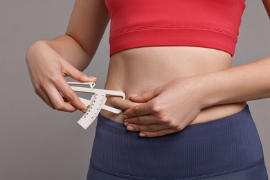 Photo of Woman measuring body fat with caliper on gray background, closeup