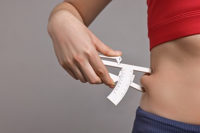 Photo of Woman measuring body fat with caliper on gray background, closeup