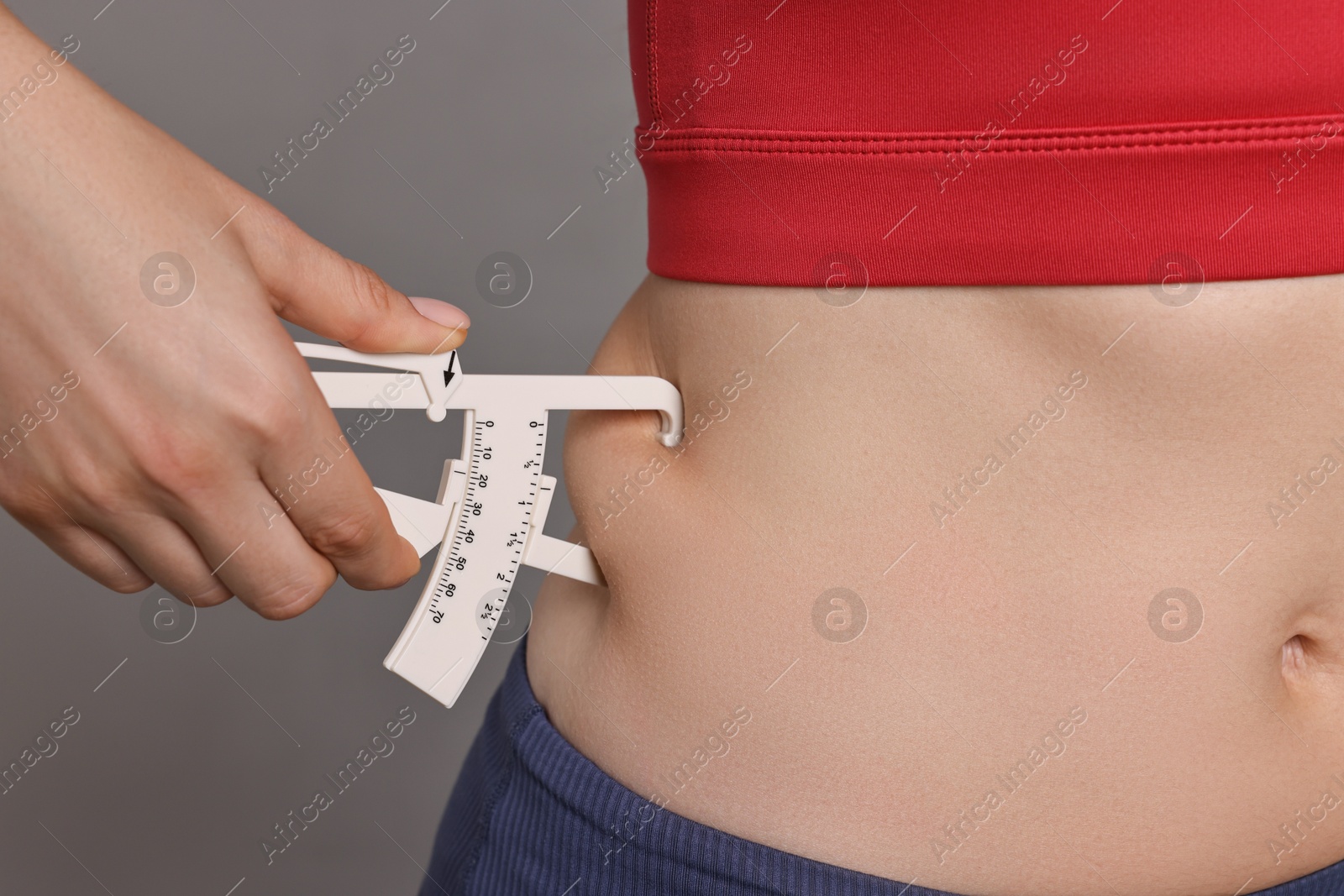 Photo of Woman measuring body fat with caliper on gray background, closeup