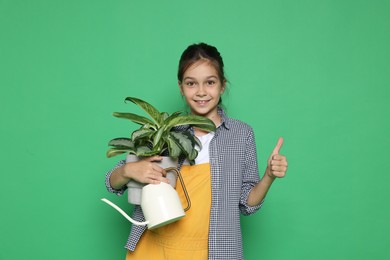 Girl with watering can and potted plant pretending to be gardener on green background. Dreaming of future profession