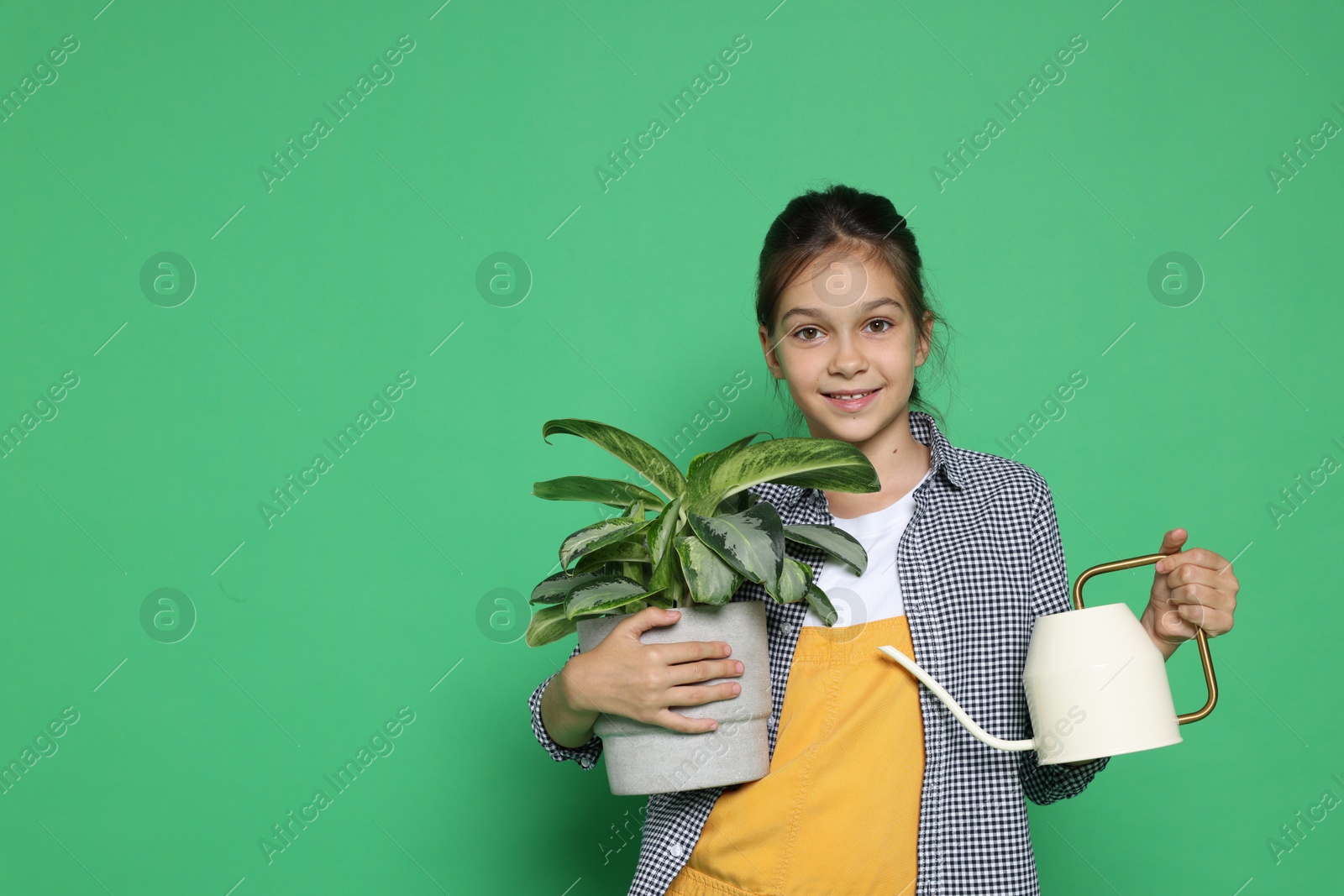 Photo of Girl with watering can and potted plant pretending to be gardener on green background. Dreaming of future profession