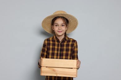 Girl with straw hat and wooden crate pretending to be farmer on light grey background. Dreaming of future profession