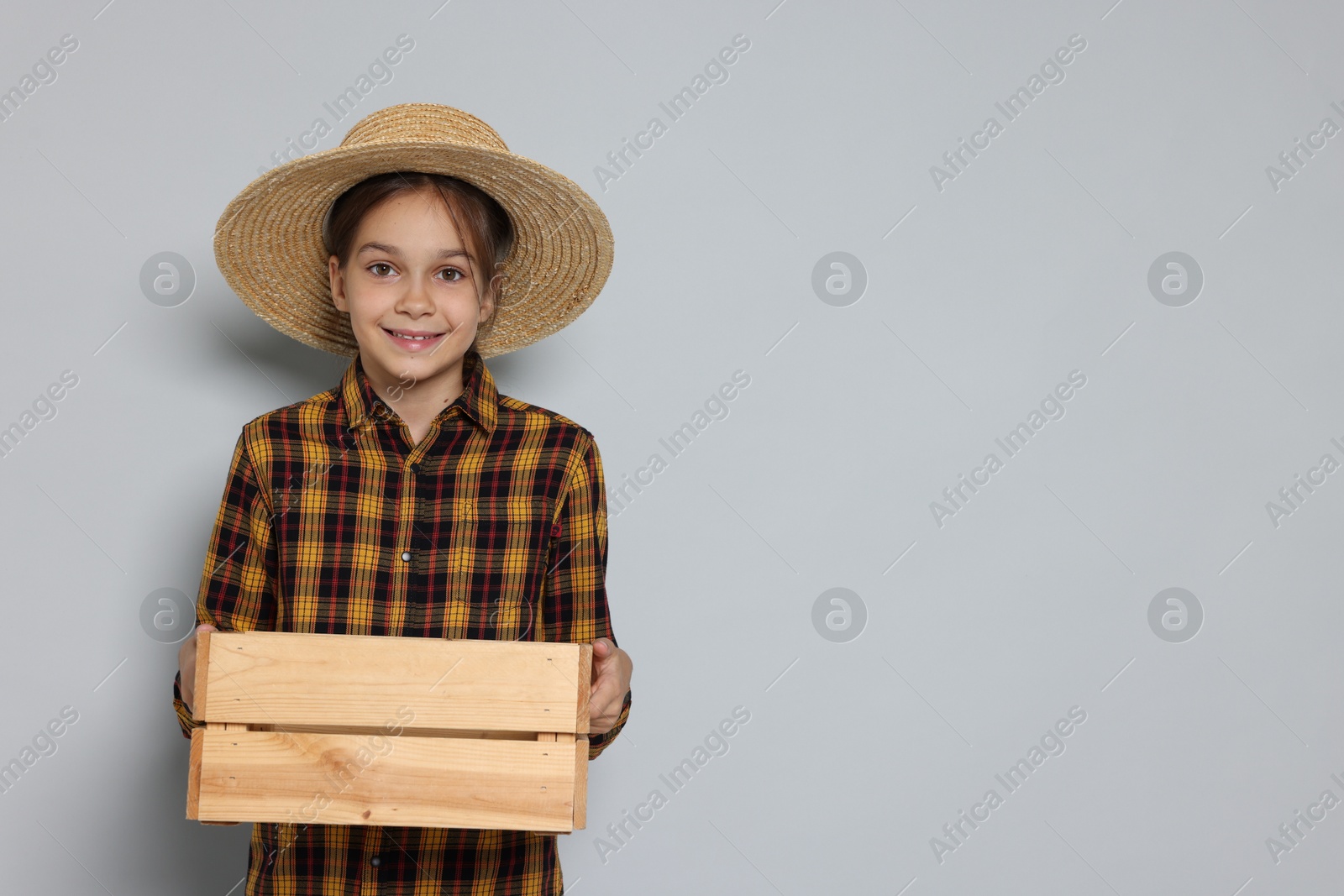 Photo of Girl with straw hat and wooden crate pretending to be farmer on light grey background, space for text. Dreaming of future profession