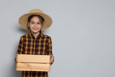 Girl with straw hat and wooden crate pretending to be farmer on light grey background, space for text. Dreaming of future profession