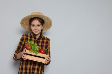 Photo of Girl with straw hat, wooden crate and vegetables pretending to be farmer on light grey background, space for text. Dreaming of future profession