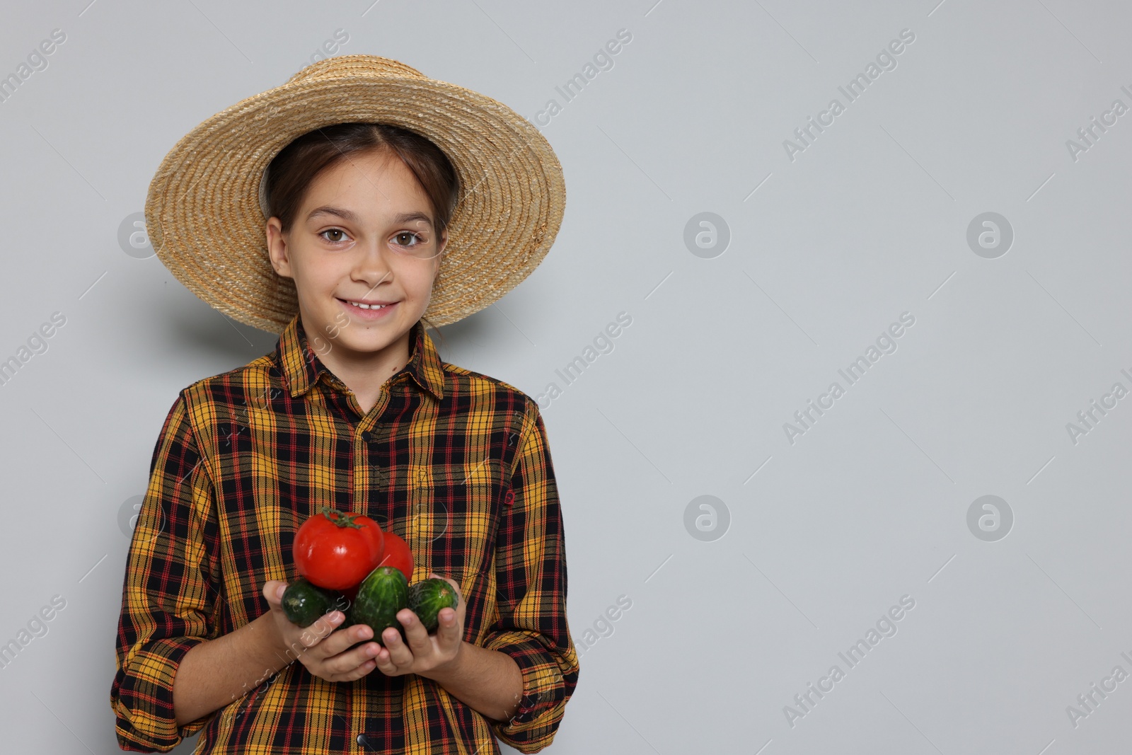 Photo of Girl with straw hat and vegetables pretending to be farmer on light grey background, space for text. Dreaming of future profession