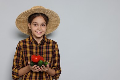 Girl with straw hat and vegetables pretending to be farmer on light grey background, space for text. Dreaming of future profession