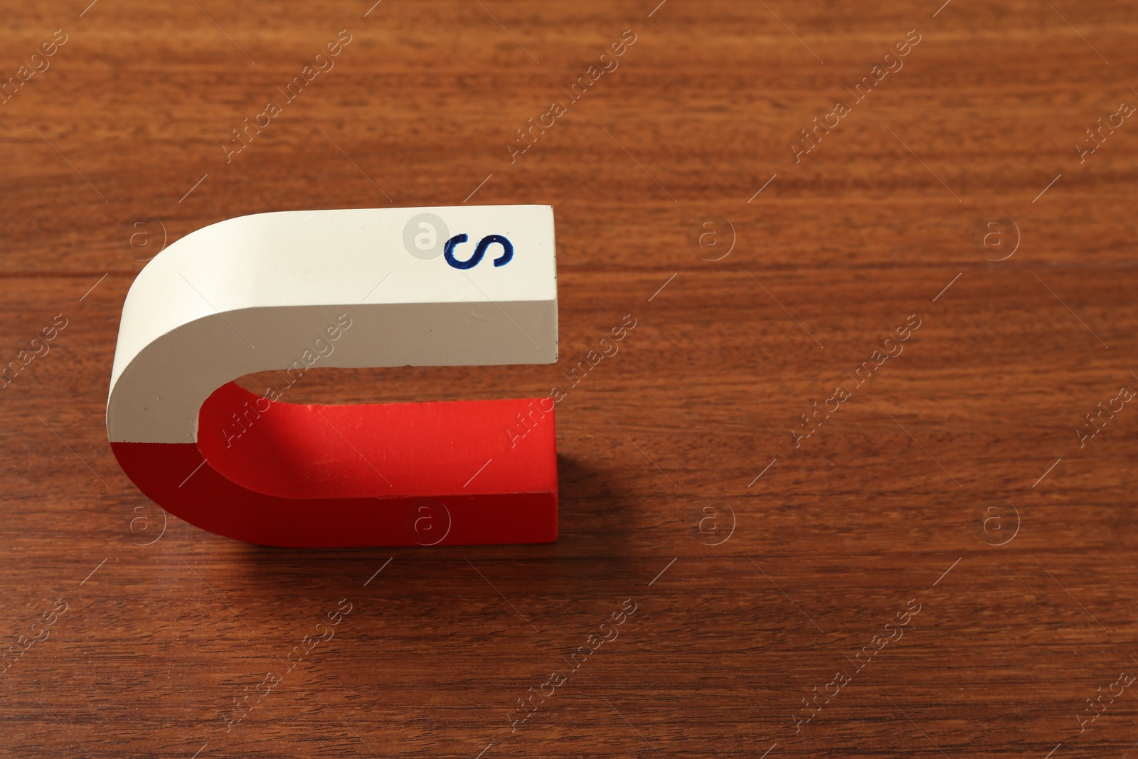 Photo of One horseshoe magnet on wooden table. Space for text