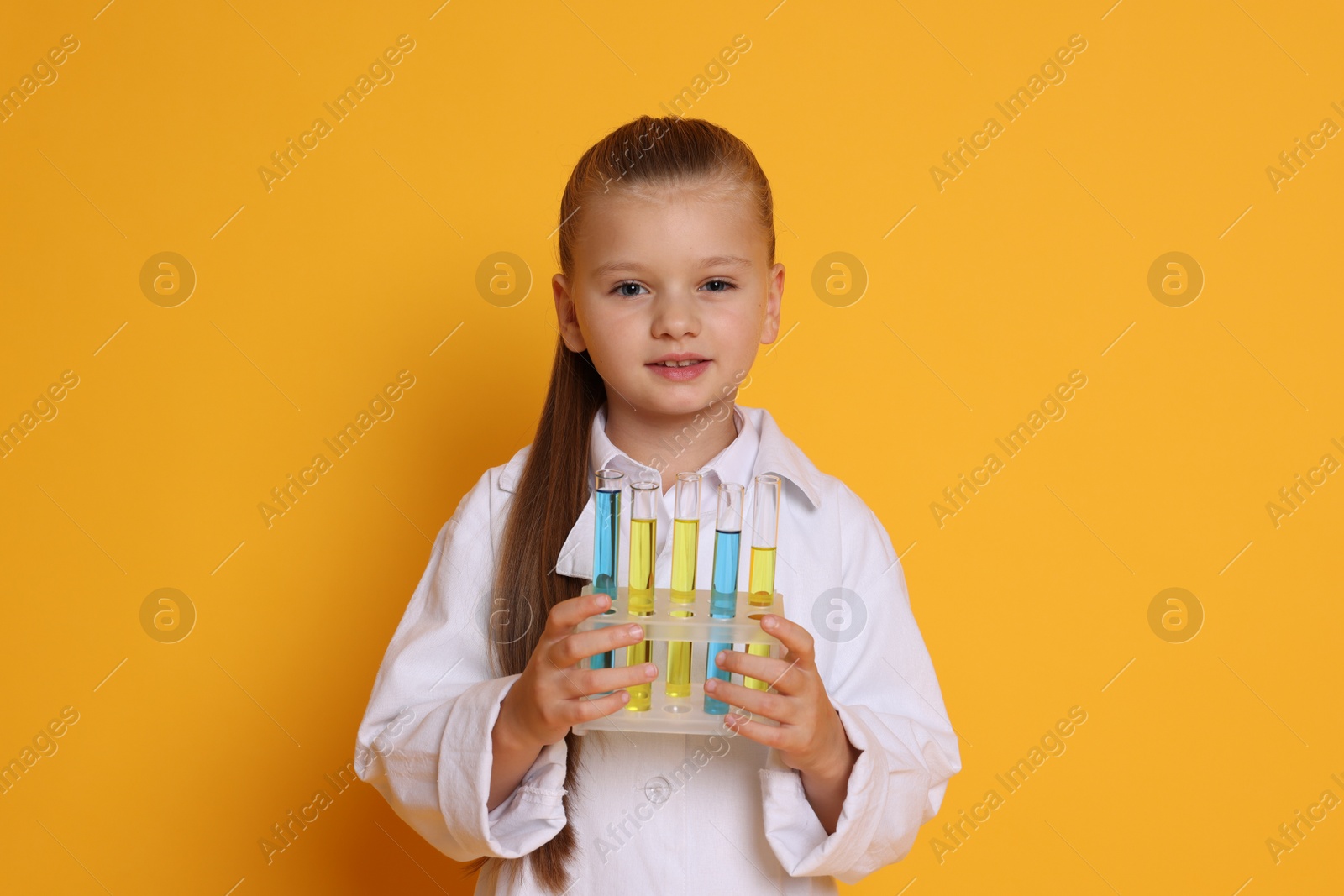 Photo of Little girl with test tubes pretending to be scientist on orange background. Dreaming of future profession