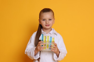 Photo of Little girl with test tubes pretending to be scientist on orange background. Dreaming of future profession