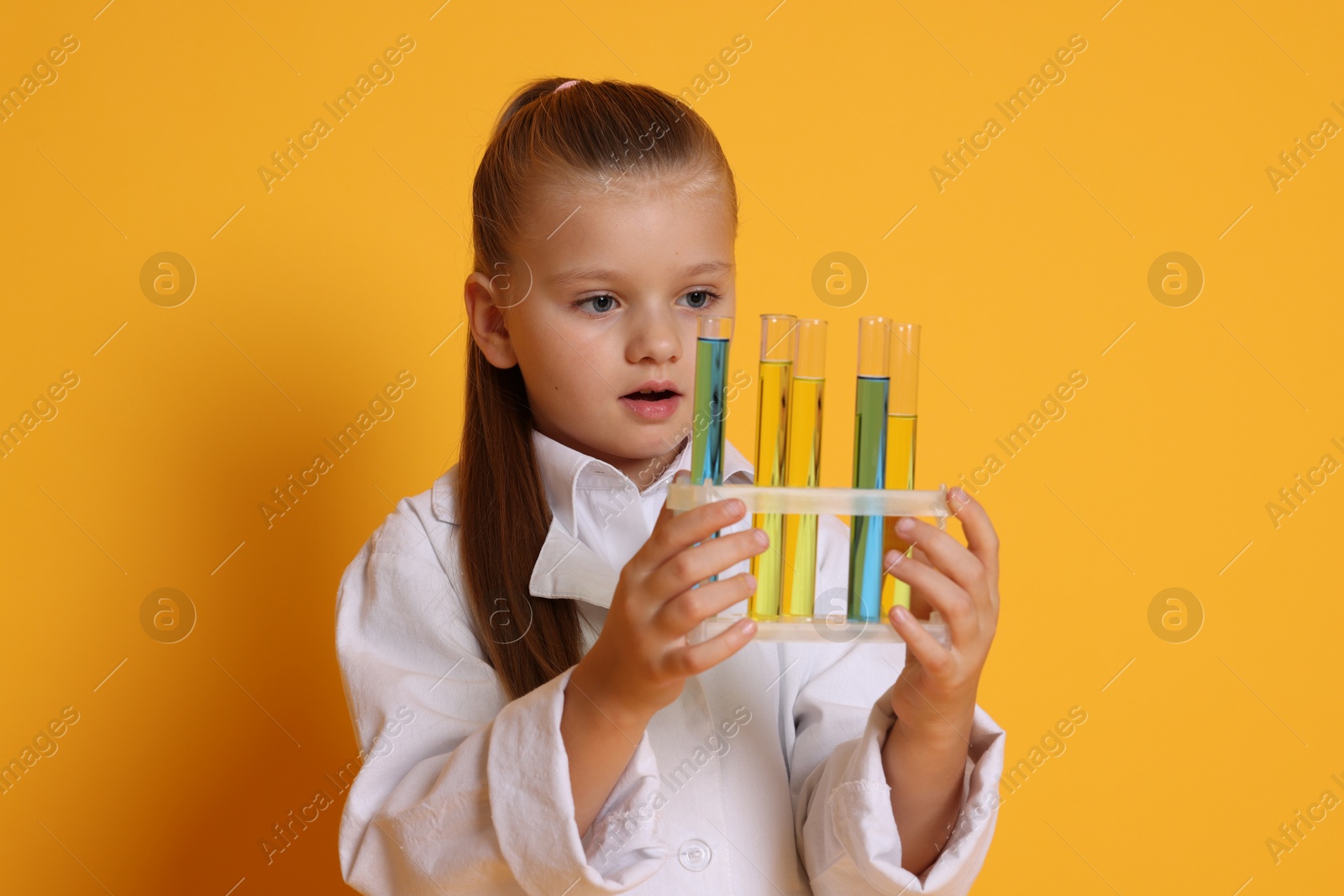 Photo of Little girl with test tubes pretending to be scientist on orange background. Dreaming of future profession