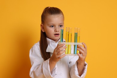 Little girl with test tubes pretending to be scientist on orange background. Dreaming of future profession