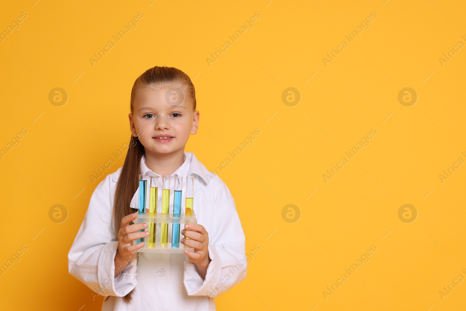 Photo of Little girl with test tubes pretending to be scientist on orange background, space for text. Dreaming of future profession