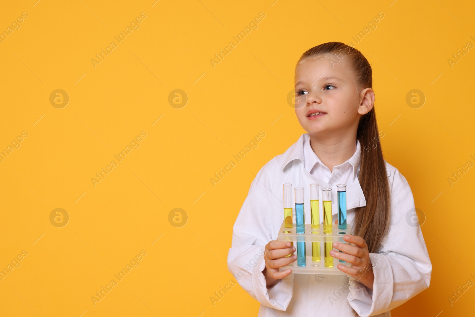 Photo of Little girl with test tubes pretending to be scientist on orange background, space for text. Dreaming of future profession